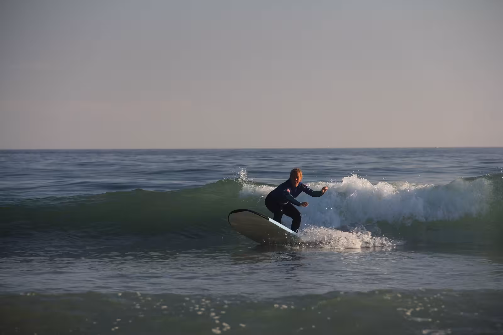Beginner surfer catching a small green wave during a sunset surf lesson clinic on a calm ocean beach