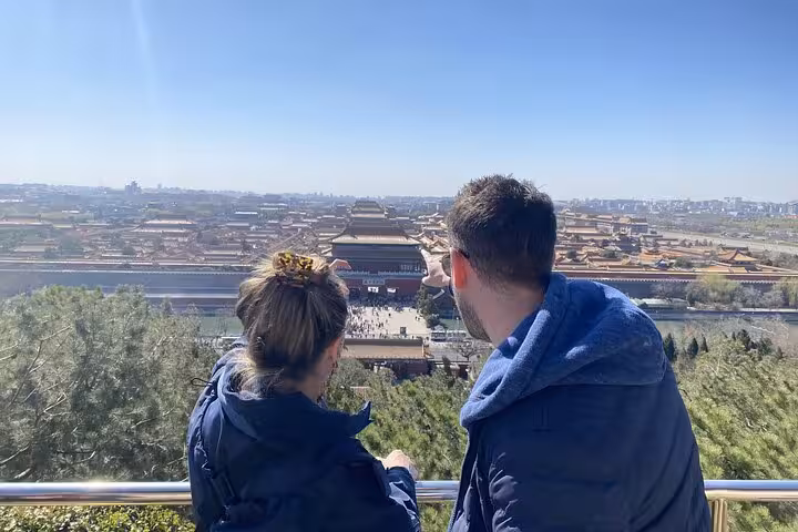 Tourists admiring the panoramic view of the Forbidden City from a Beijing vantage point on a clear day.