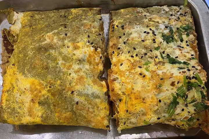Close-up of savory Jianbing pancakes topped with sesame seeds and scallions on a Beijing food tour.