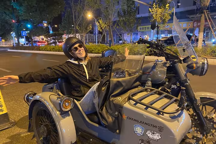 Excited traveler enjoying a night ride in a vintage sidecar on the illuminated streets of Beijing.