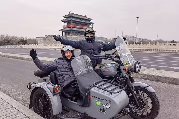 Two people enjoying a sidecar ride in Beijing near a historic gate, bundled up for the winter weather.