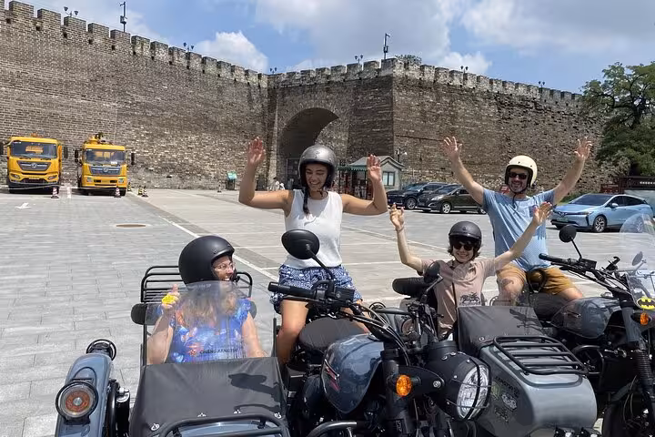 Tourists enjoy a thrilling Beijing sidecar tour, posing with joy in front of historic city walls under a sunny sky.