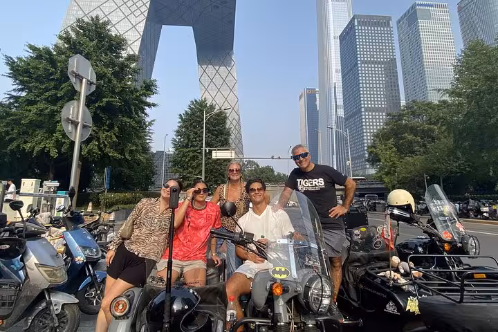 Group of tourists pose with sidecars in front of modern skyscrapers on a Beijing tour.