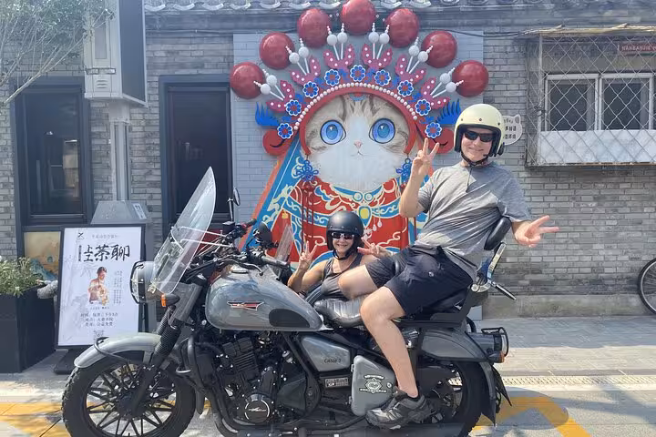 Travelers pose on a sidecar in front of a colorful cat mural during a Beijing exploration tour.