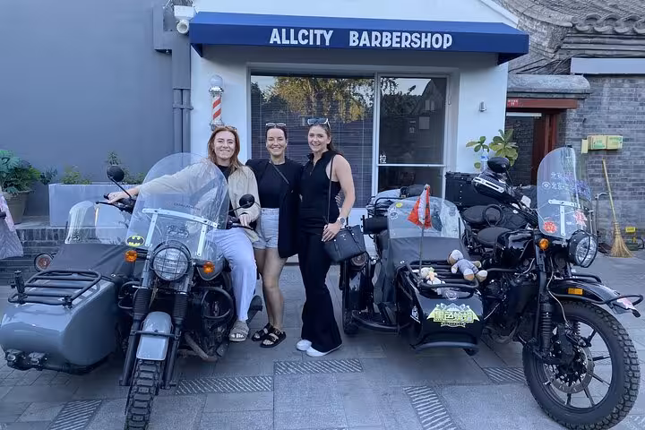 Three women smiling beside sidecars at a barbershop in Beijing, showcasing a unique city tour experience.