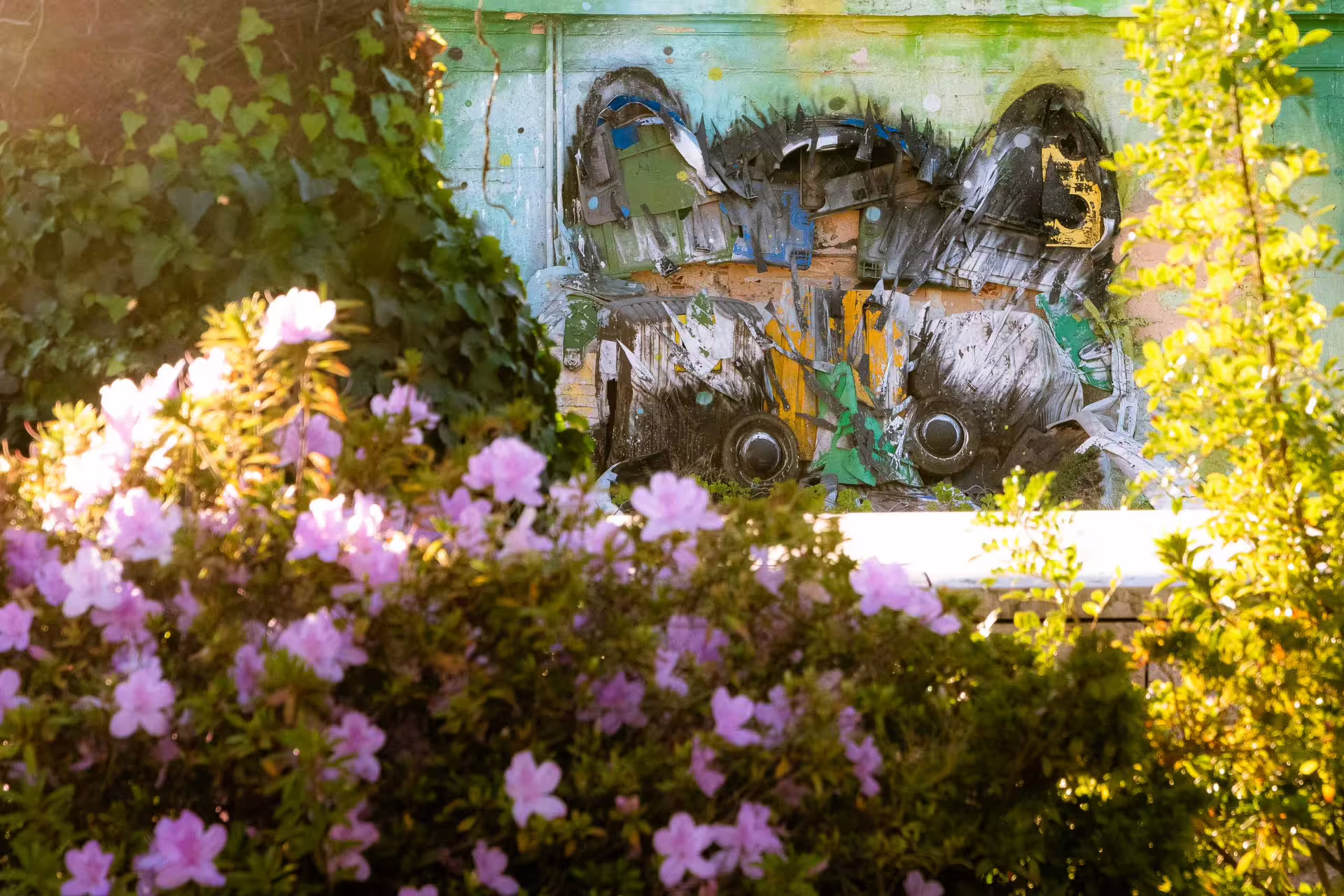 Colorful street art mural partially hidden by vibrant flowers and ivy during a scenic Belém sunset photography walk in Lisbon.