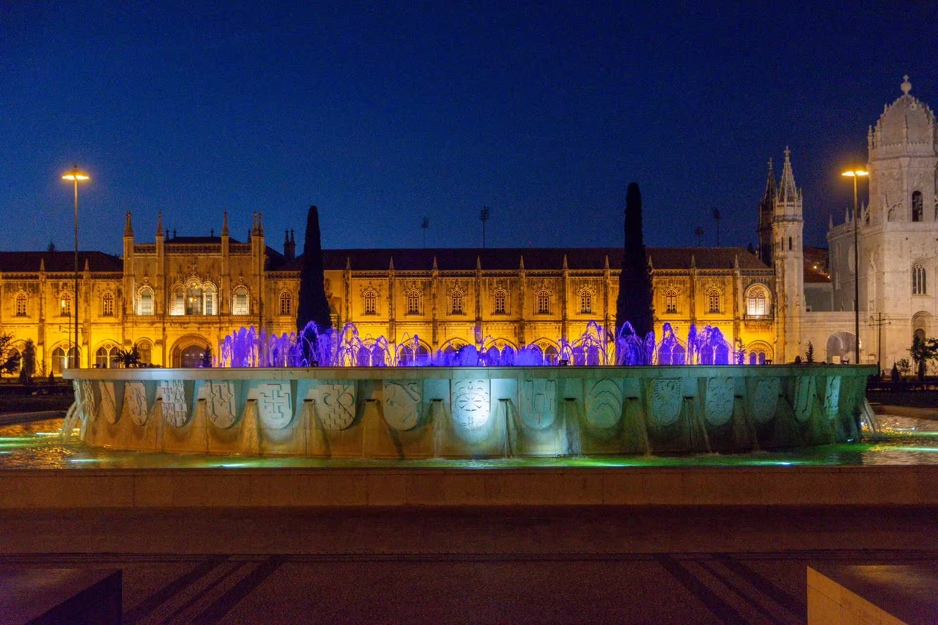 Illuminated fountain and historic architecture glow under a vibrant evening sky during the Belém Sunset Photography Walk in Lisbon.