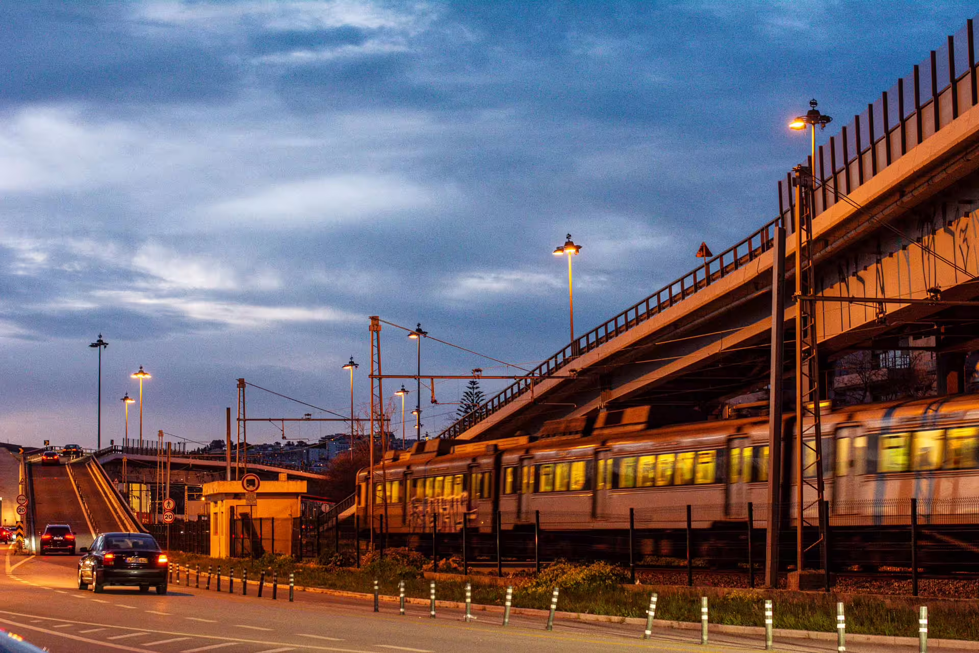 Evening view of a train passing under a bridge and cars on a road during a Belém Sunset Photography Walk in Lisbon.