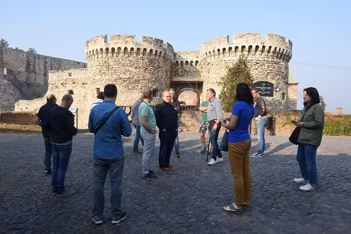 Tour group exploring the historic stone walls of Belgrade Fortress under clear blue skies.