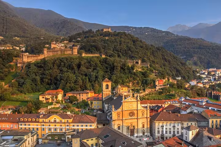 Scenic view of Bellinzona's medieval castles nestled in lush green hills under a clear blue sky in Ticino.