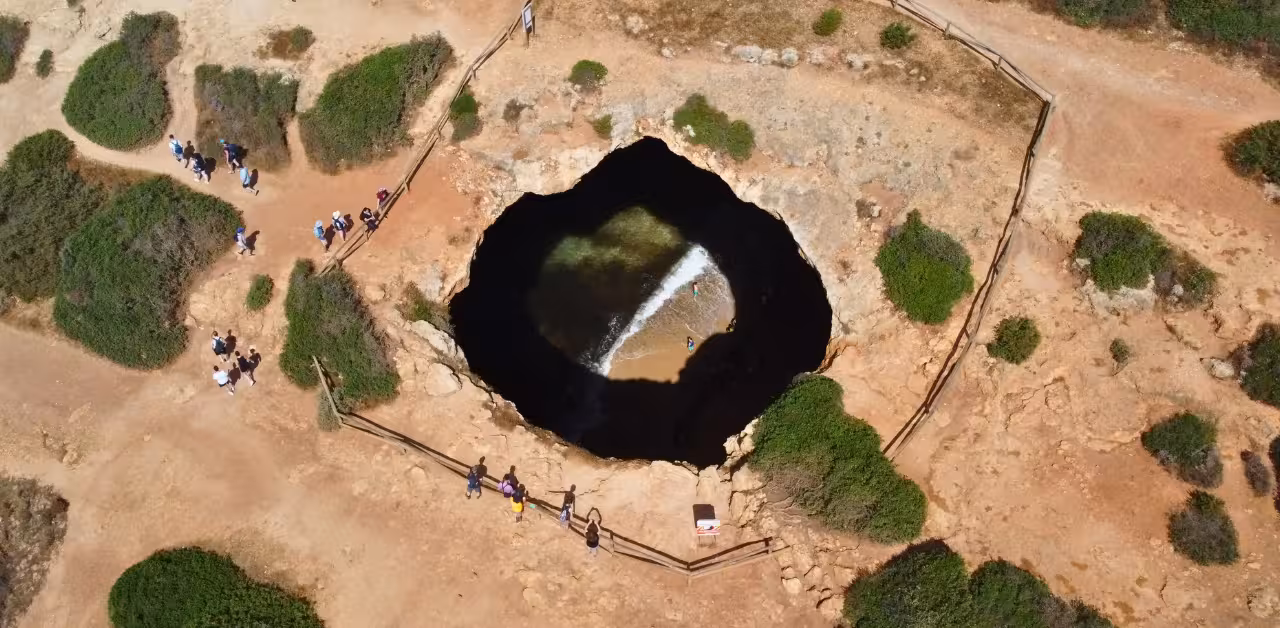 Aerial view of Benagil Cave sinkhole revealing hidden beach and turquoise water beneath coastal cliffs in Algarve, Portugal