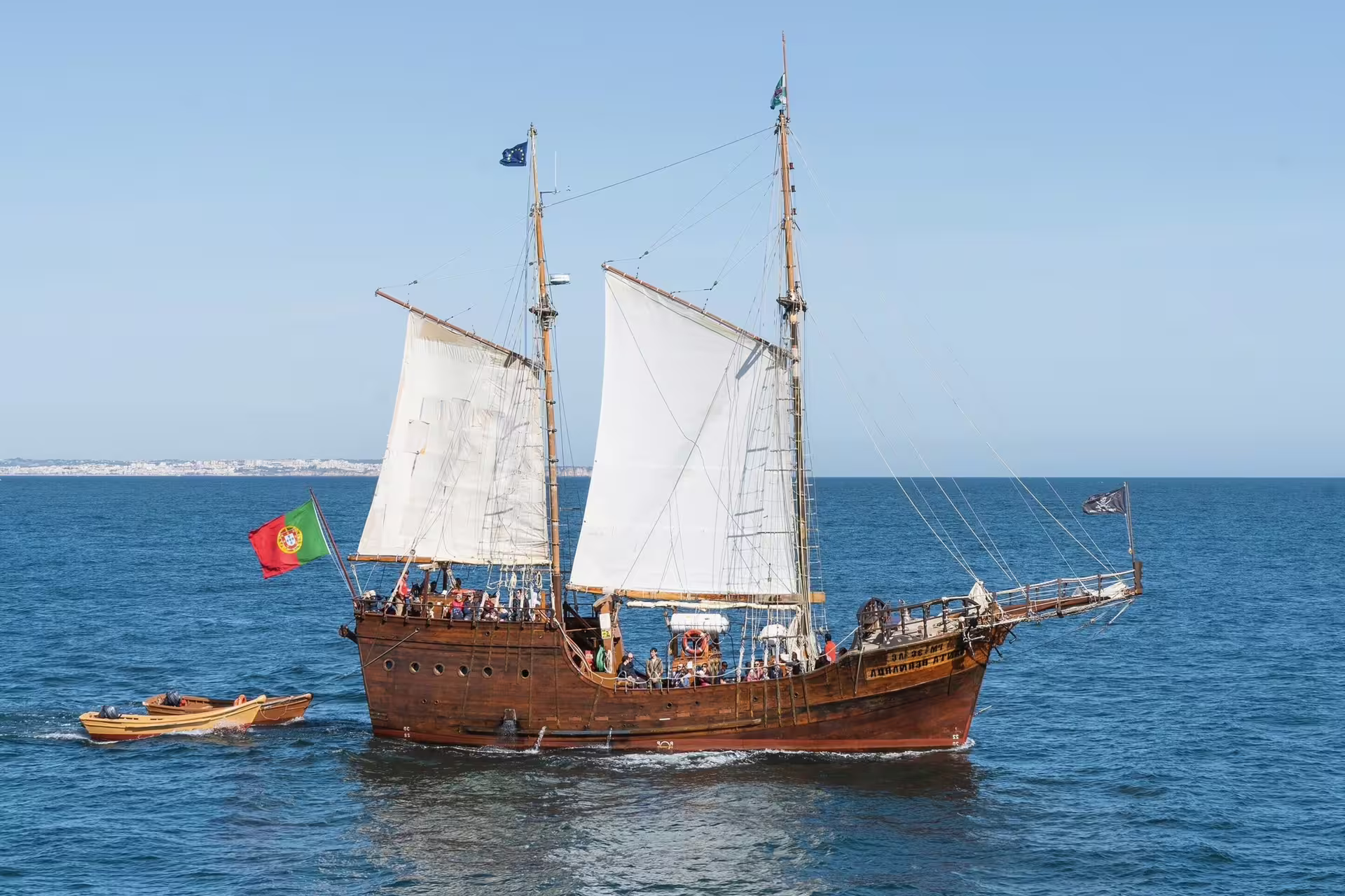 Portuguese flag-waving on a classic wooden sailboat navigating the Algarve coast, perfect for Benagil cave tours.