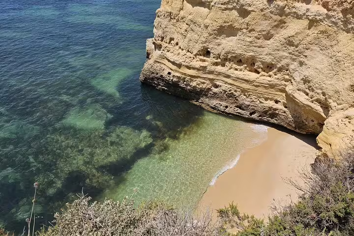 Scenic view of a secluded beach with crystal-clear waters and rocky cliffs on the Algarve Coast near Benagil Cave.
