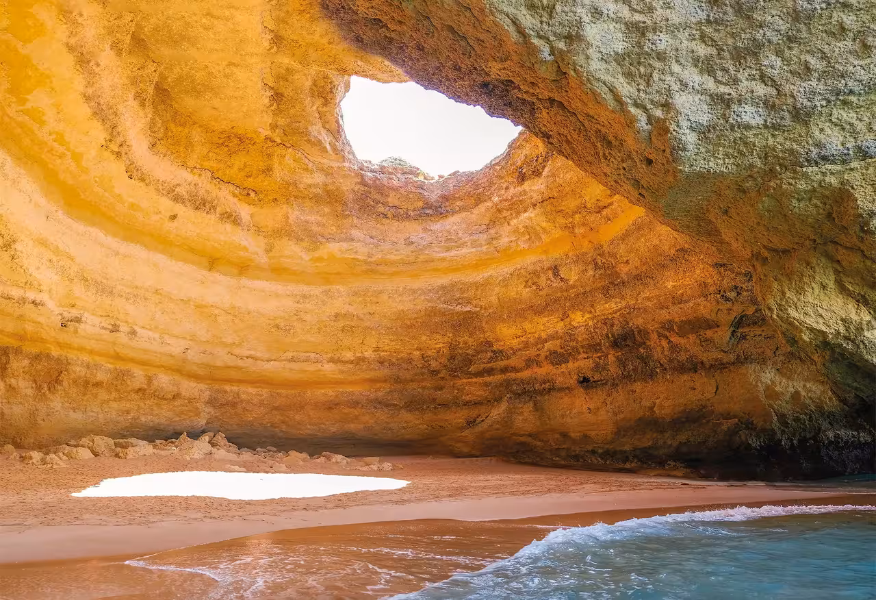 Interior of iconic Benagil Cave in Algarve Portugal with a stunning natural skylight opening above a sandy beach and turquoise waves