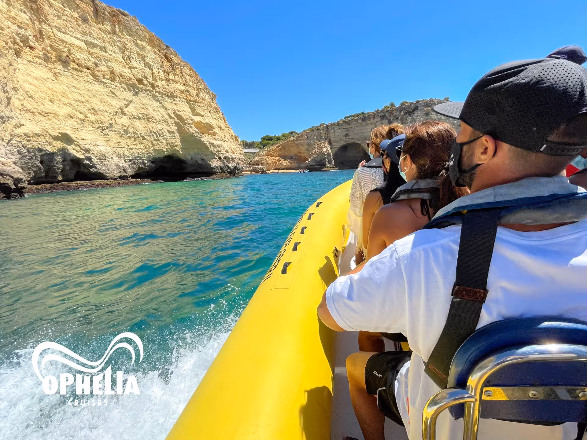 Tourists on a yellow boat approaching the scenic cliffs of Benagil Cave under a bright blue sky in Algarve, Portugal.
