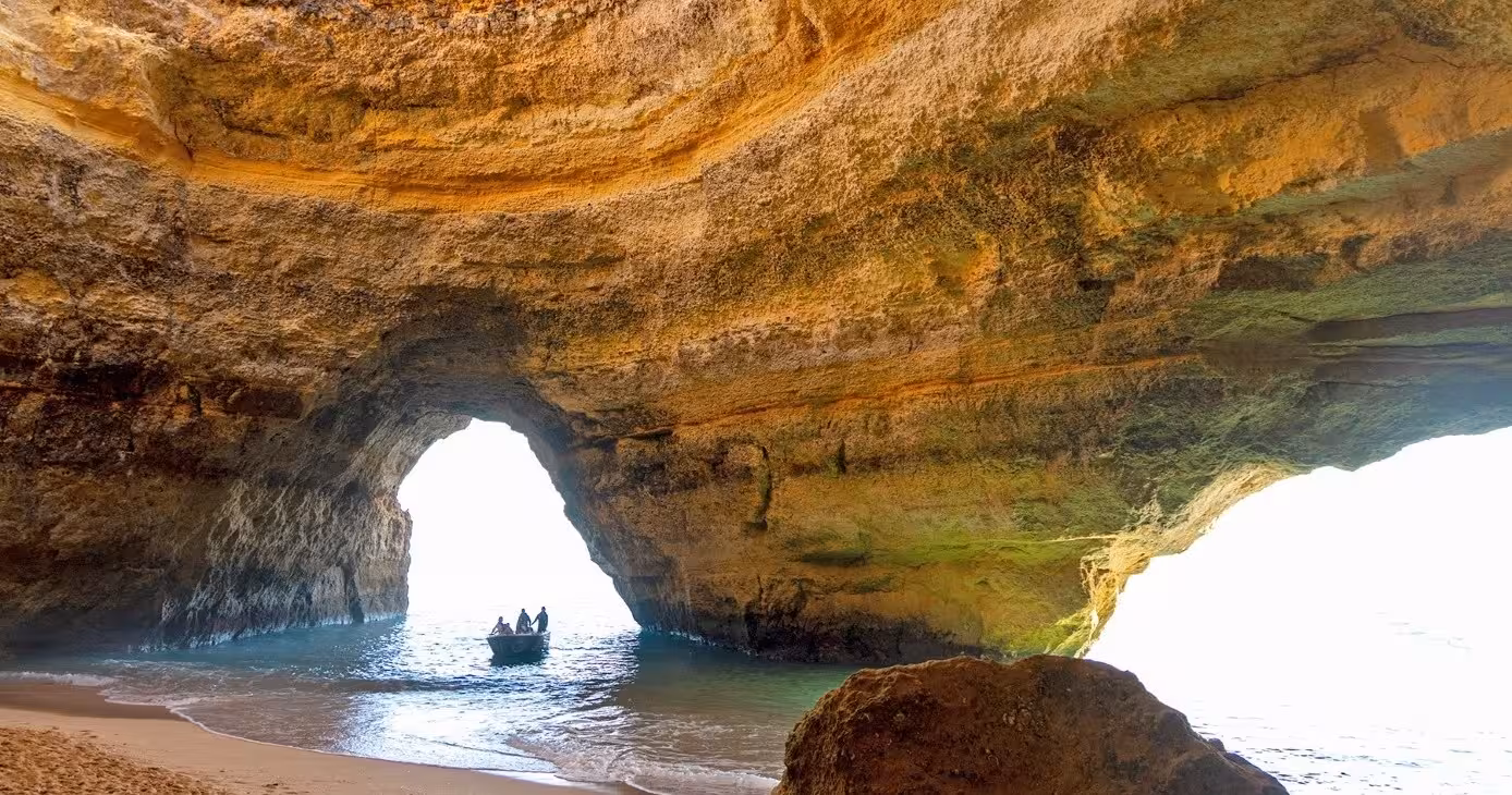 Small boat entering the famous Benagil cave in Algarve, Portugal, revealing its vast arched ceiling and sandy shore