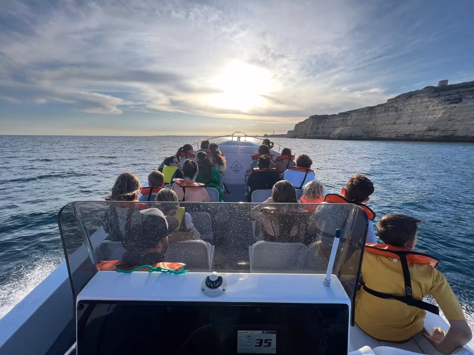 Group enjoying a Benagil Cave coastal boat tour at sunset, speeding past Algarve cliffs on calm Atlantic Ocean waters.