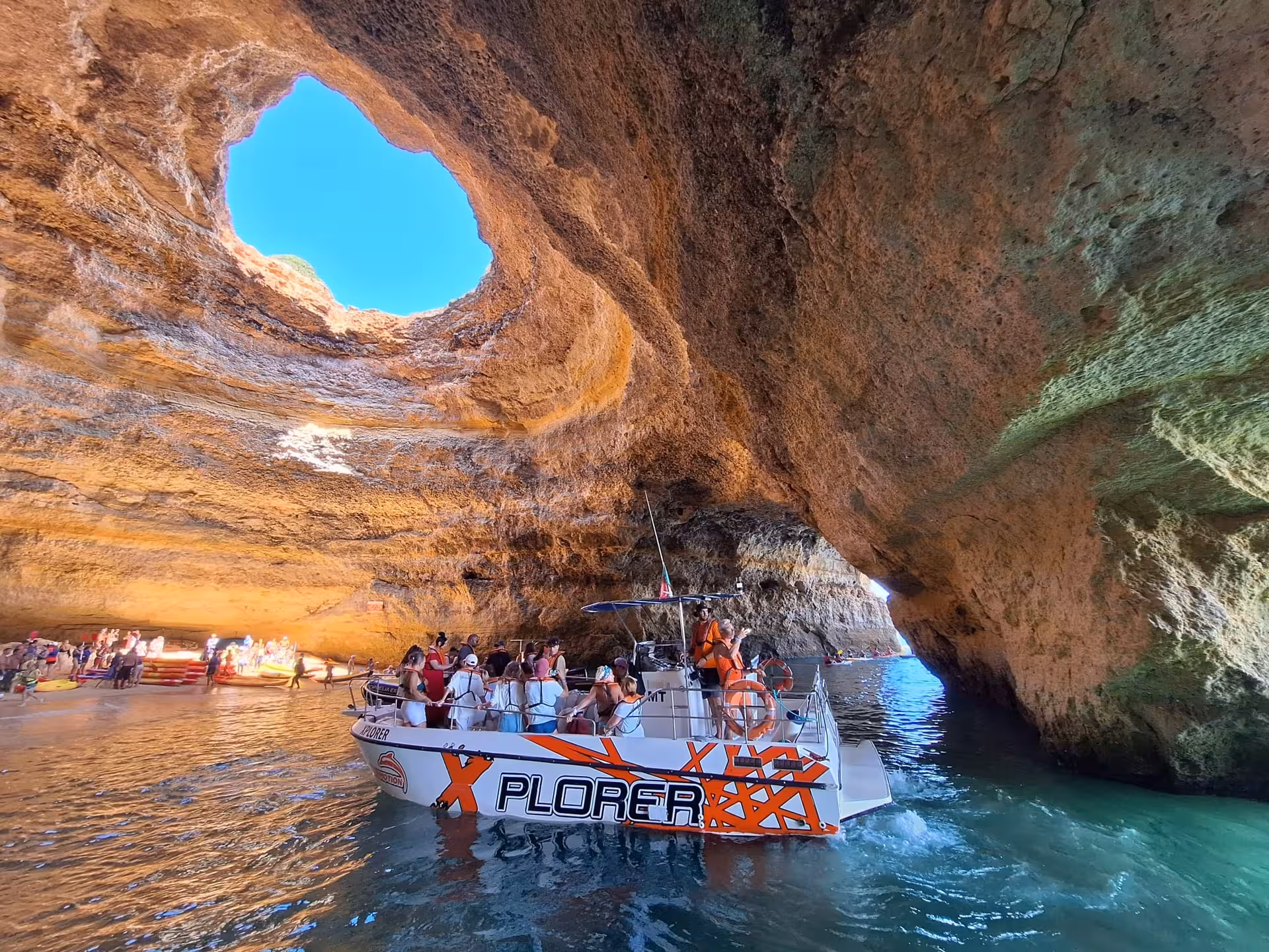 Small cruise boat enters Benagil cave on Algarve coast, showcasing sea cave ceilings, turquoise water and guided tour guests