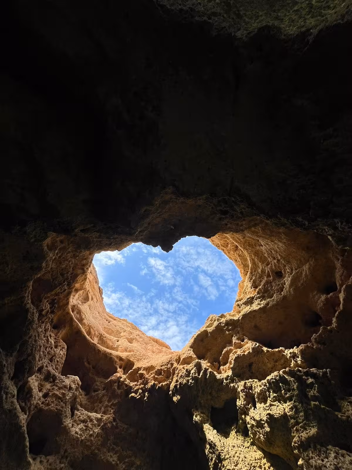 View of blue sky through natural heart-shaped skylight inside Benagil Cave on a private Algarve sea cave tour
