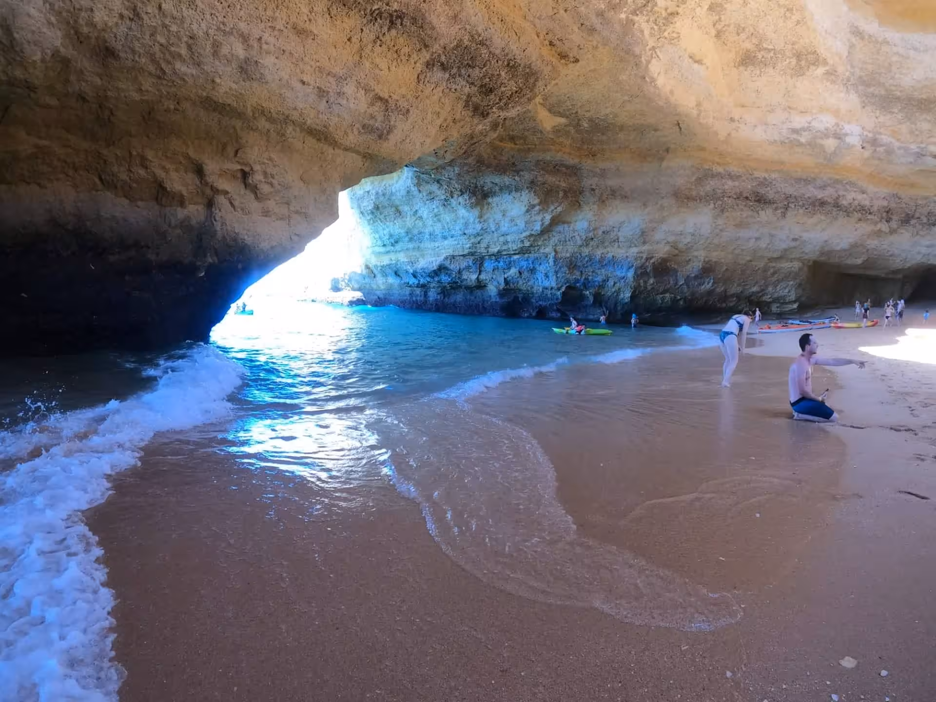 Visitors relax on the sandy beach inside Benagil cave as gentle Atlantic waves roll in during Algarve kayak excursion