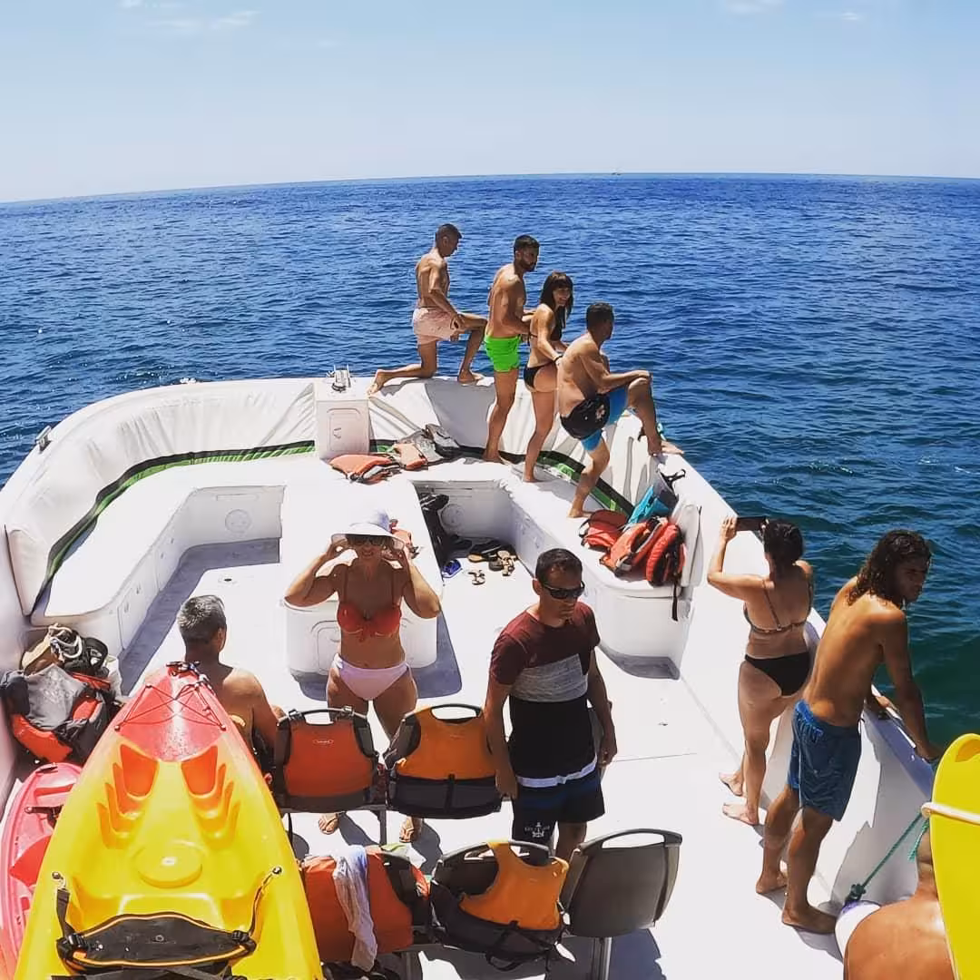 Group of travelers on support boat with kayaks and life jackets preparing to start Benagil cave kayak tour in Algarve