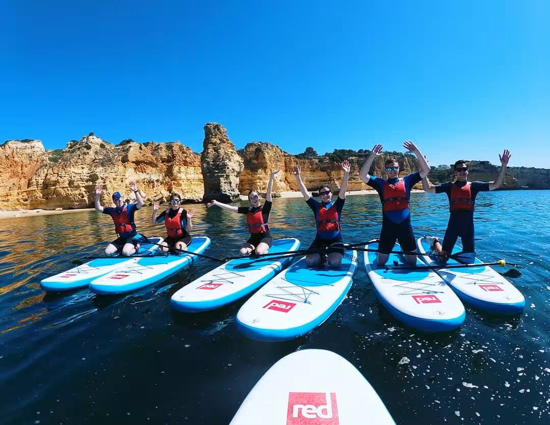 Group of friends on paddleboards raise arms while touring Benagil Cave cliffs on a guided Algarve stand-up paddle trip