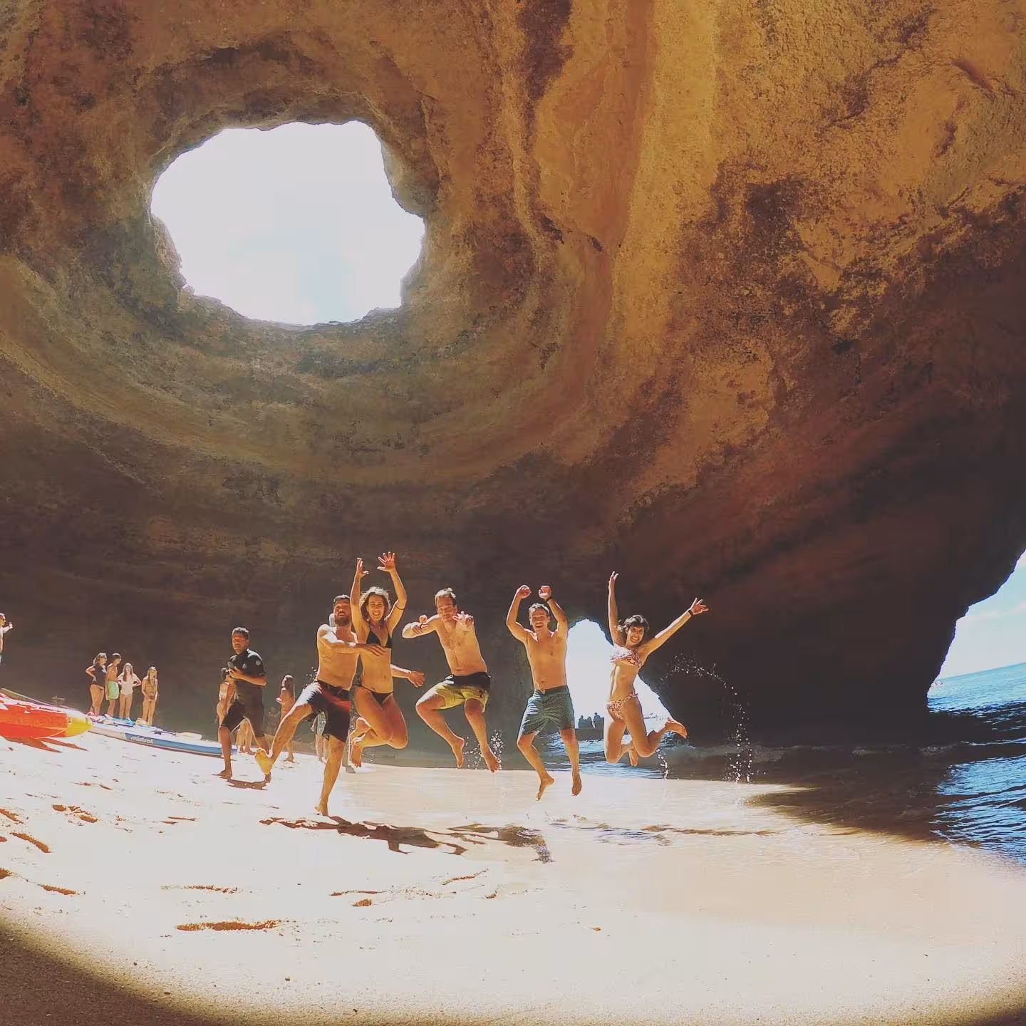 Friends jumping on the sandy beach inside Benagil Cave, enjoying a guided paddleboard and cave tour in Algarve, Portugal