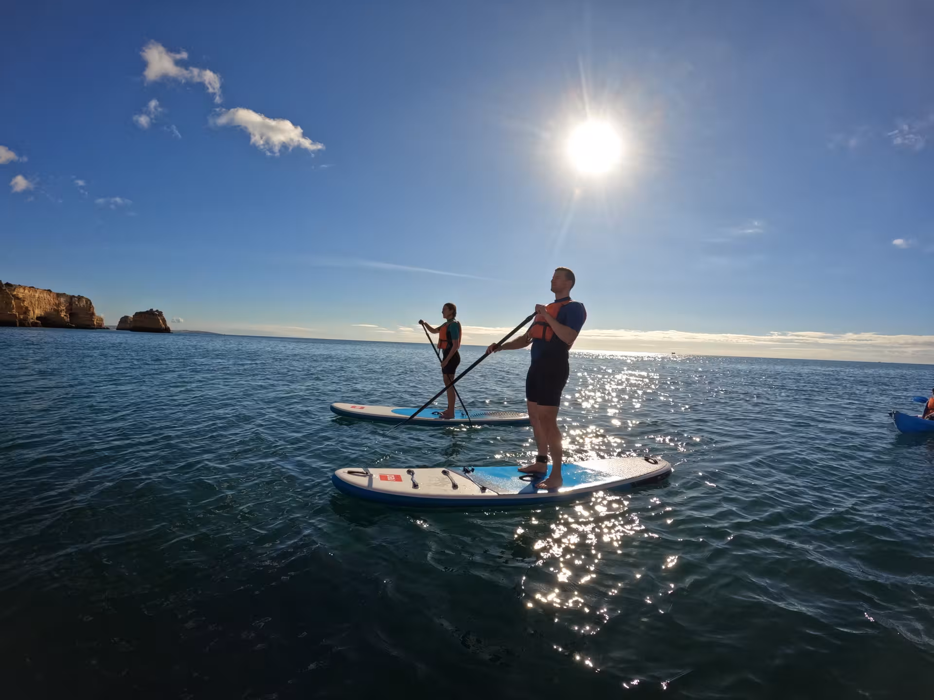 Two people stand-up paddleboarding on calm Algarve sea at sunset near Benagil cliffs during guided paddleboard experience