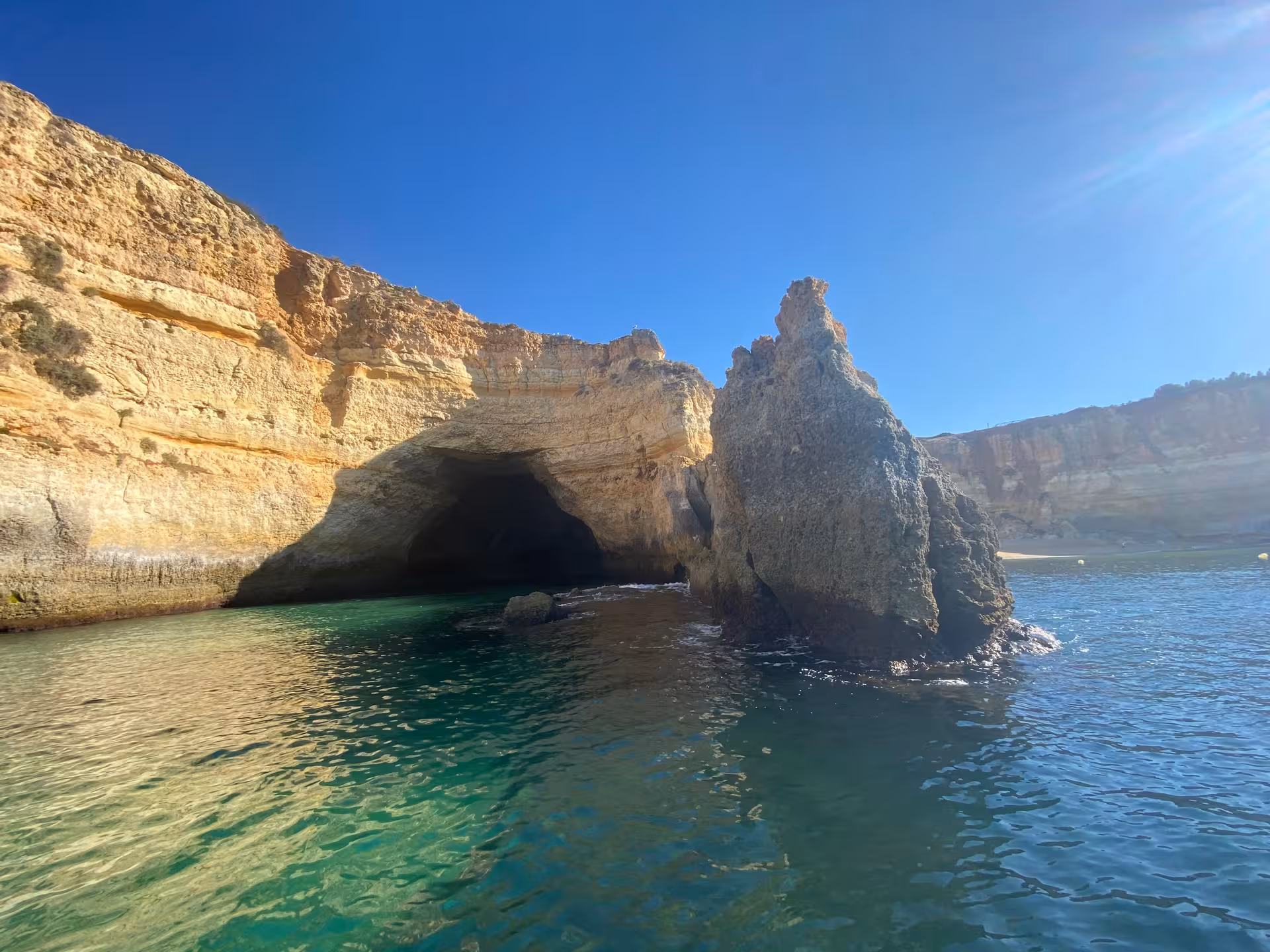 Morning sun illuminates Benagil sea cave entrance and rugged Algarve cliffs above crystal-clear Atlantic water