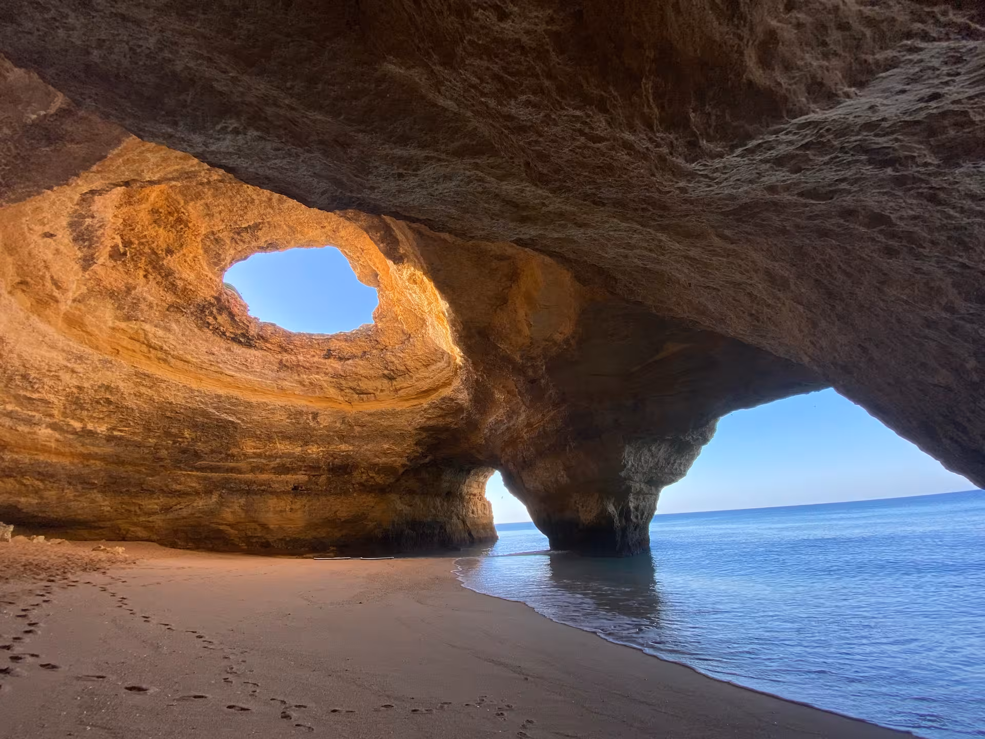 Sunrise light pours through the skylight of Benagil cave onto a secluded sandy beach and calm Atlantic waters