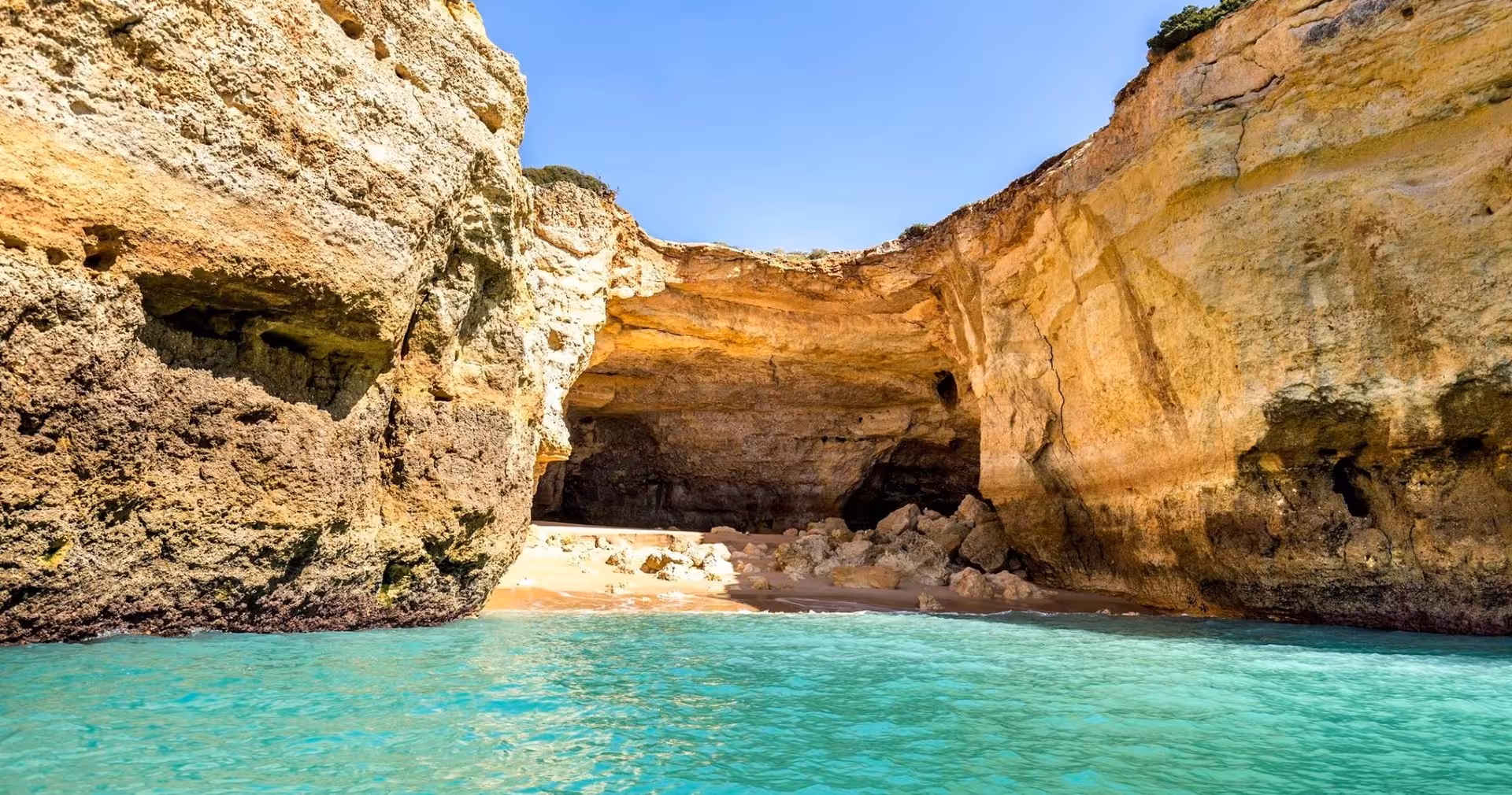 Stunning view of Benagil Cave's natural rock formation with turquoise waters and a sandy beach in Algarve, Portugal.