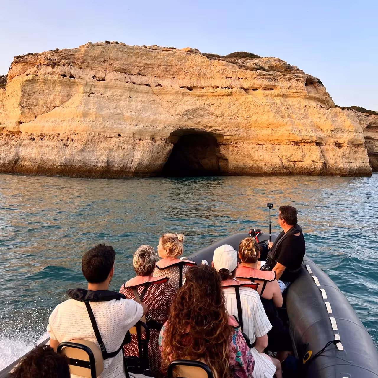 Small group on a private boat tour approaches the famous Benagil sea cave along the golden Algarve cliffs at sunset
