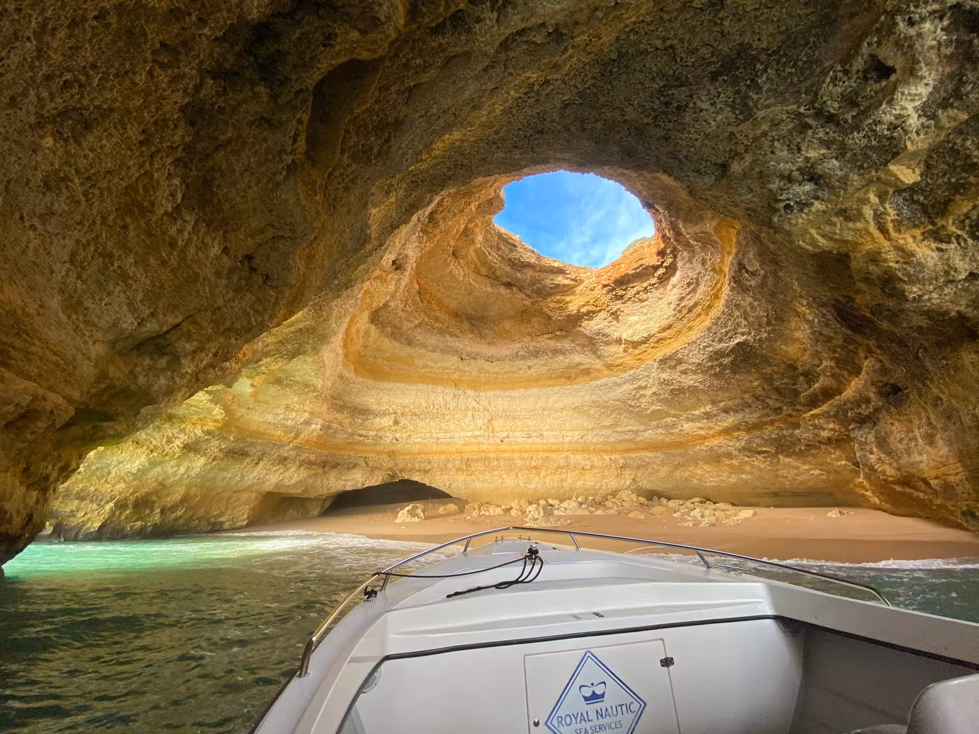 Speedboat entering Benagil Cave in Algarve, Portugal, revealing golden rock dome, sandy beach and turquoise Atlantic water