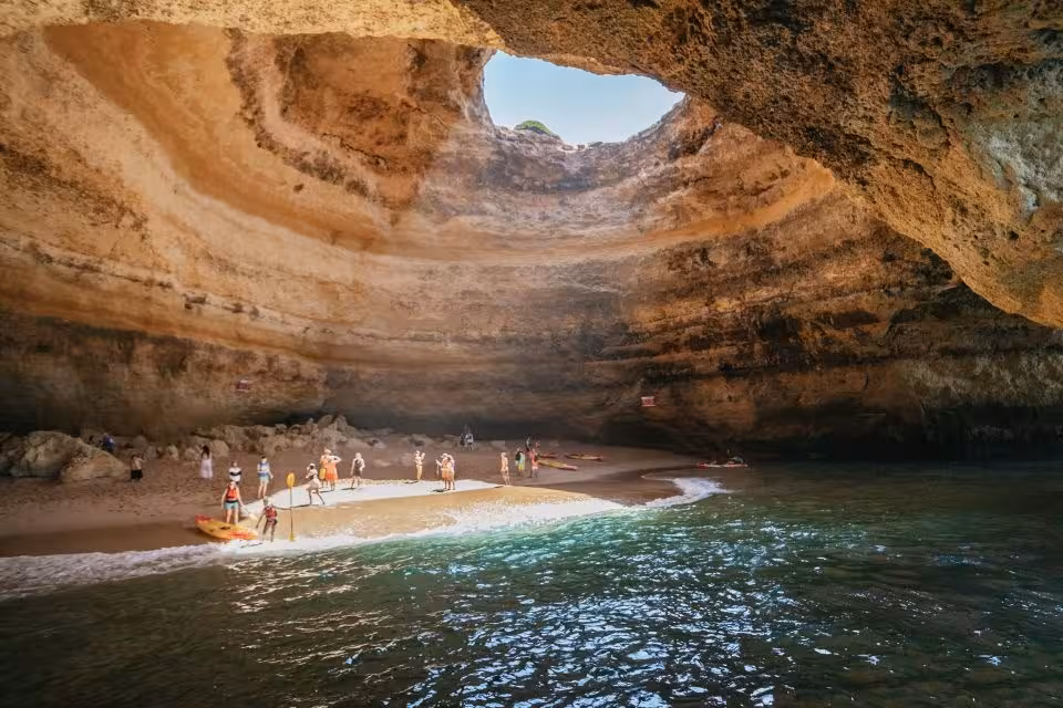 Tourists explore the sunlit interior of Benagil Cave in the Algarve, showcasing its stunning geological features.