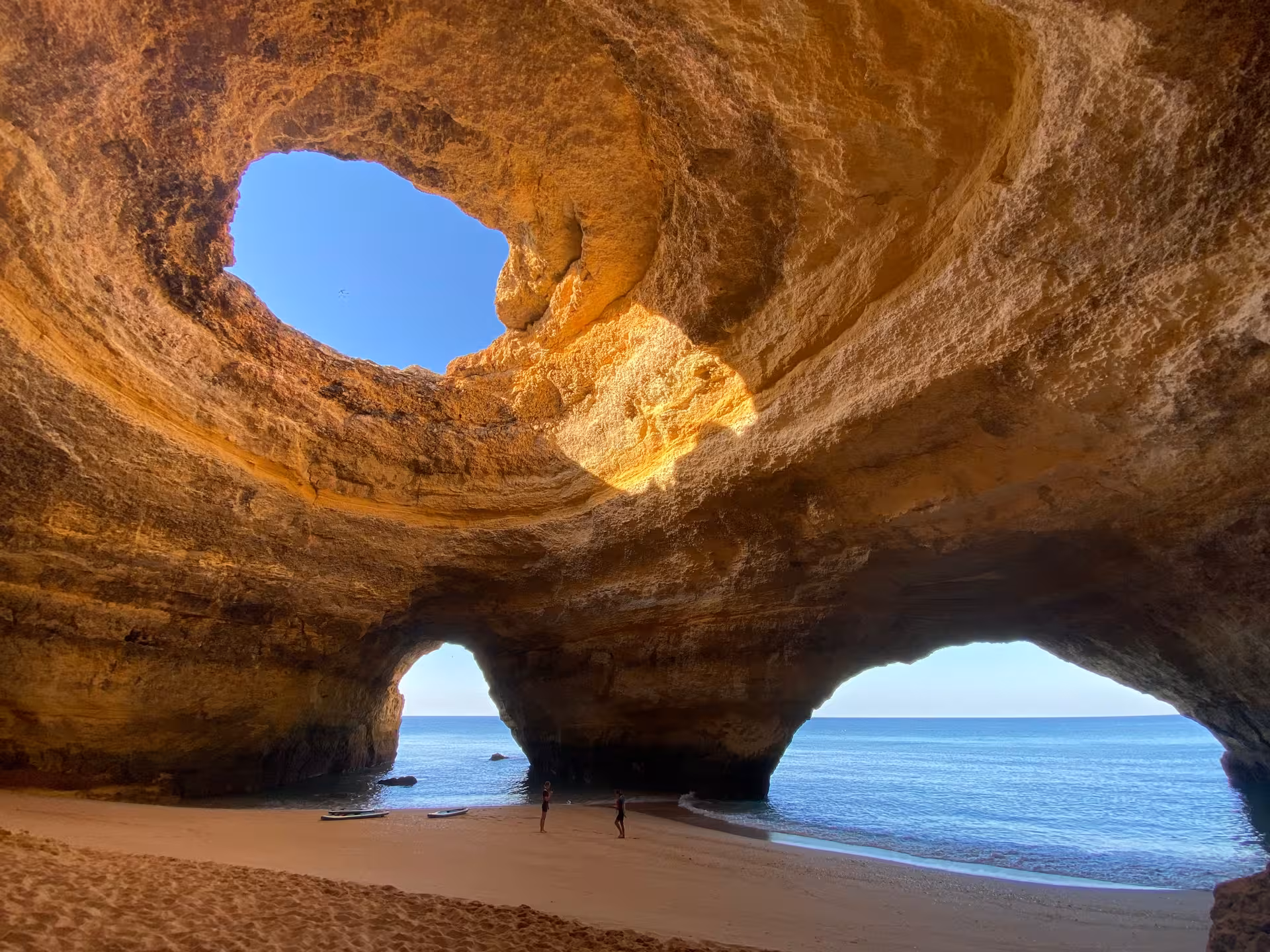 Sunrise light pours through the Benagil sea cave skylight onto golden sand and calm Algarve waters, a hidden Portugal gem