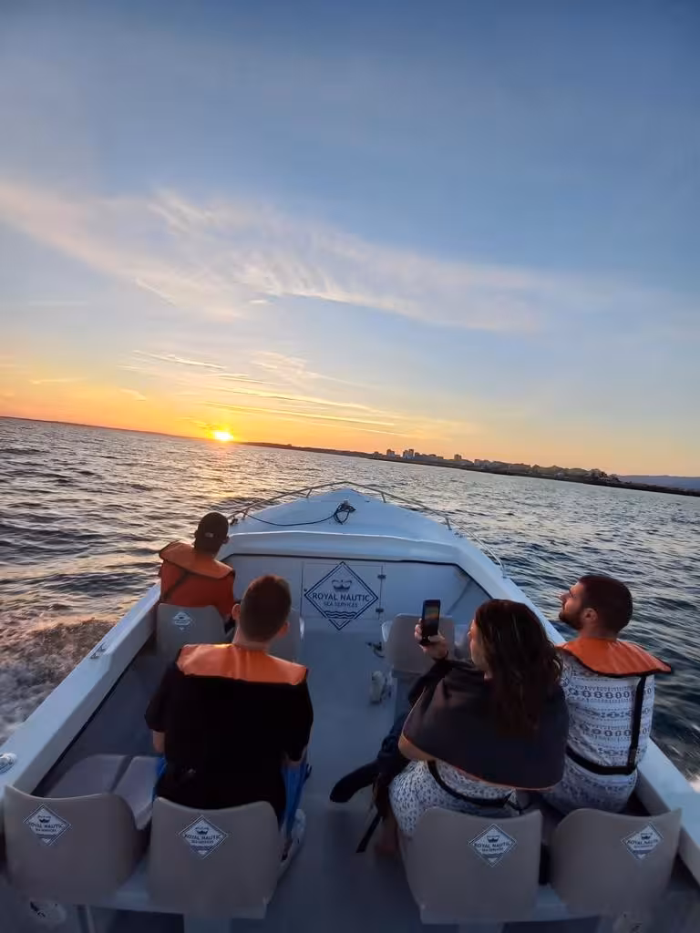 Small group enjoying a Benagil Cave sunset boat tour on the Algarve coast, watching the sun dip below the Atlantic horizon