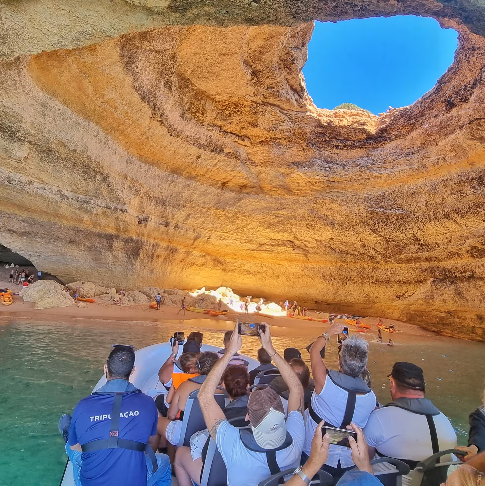 Visitors capturing the breathtaking interior of Benagil Cave, illuminated by sunlight through the natural skylight.