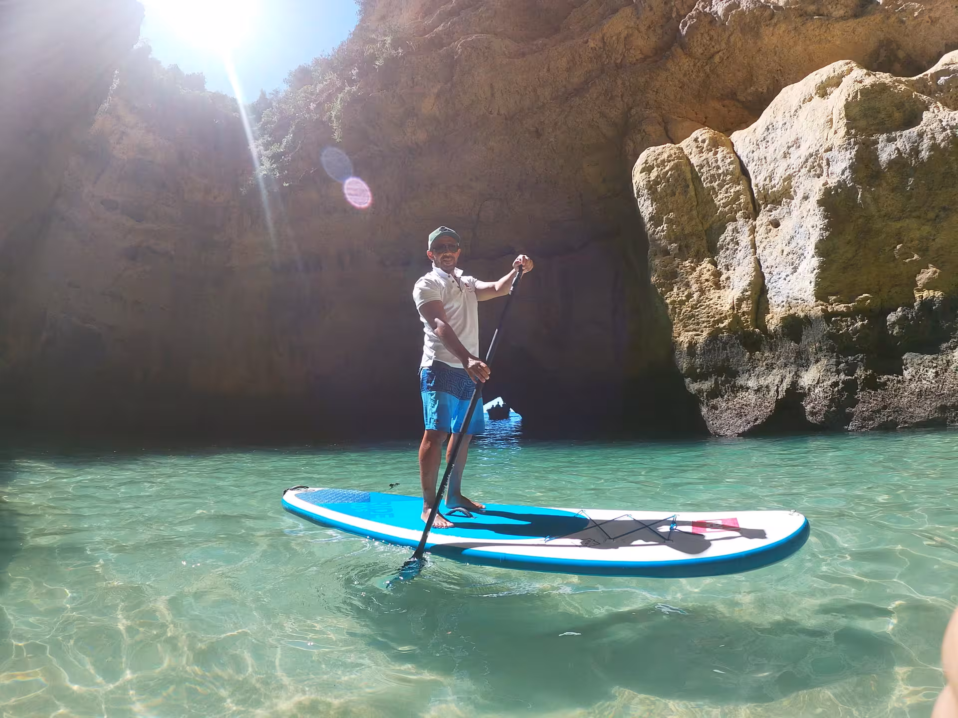 Solo paddler stands on a SUP in crystal-clear turquoise water inside Benagil Cave on a guided Algarve Portugal tour