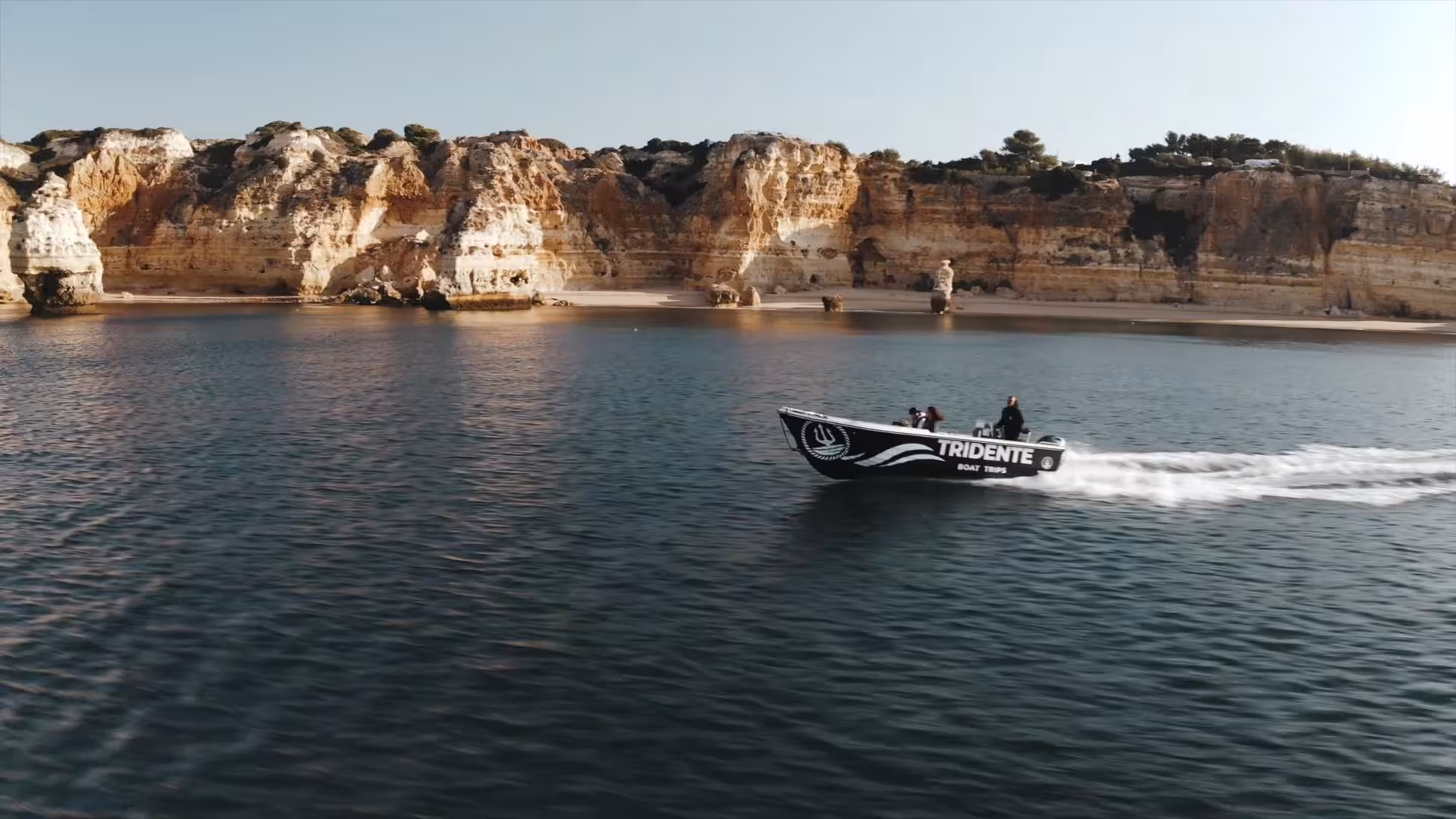 Tridente tour boat cruising along calm Atlantic waters beneath dramatic Algarve cliffs near Benagil Cave, Portugal