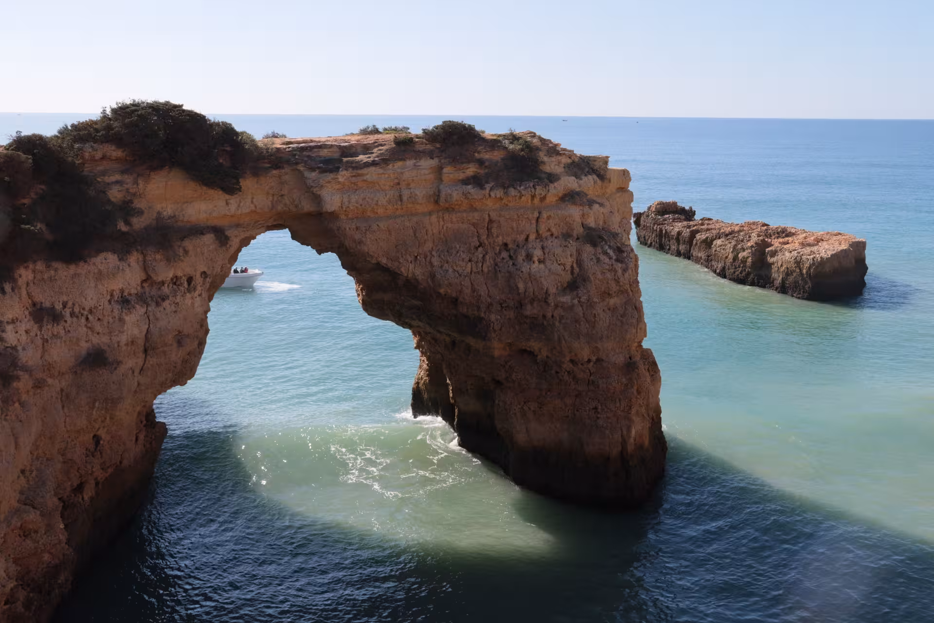Tour boat cruising through natural sea arch on Algarve coastline, en route to Benagil caves and dolphin watching adventure