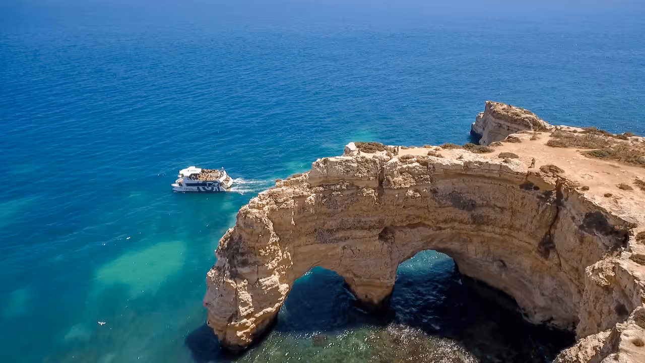 Aerial view of a guided boat tour sailing past stunning limestone rock arches along the Albufeira coast to Benagil Caves