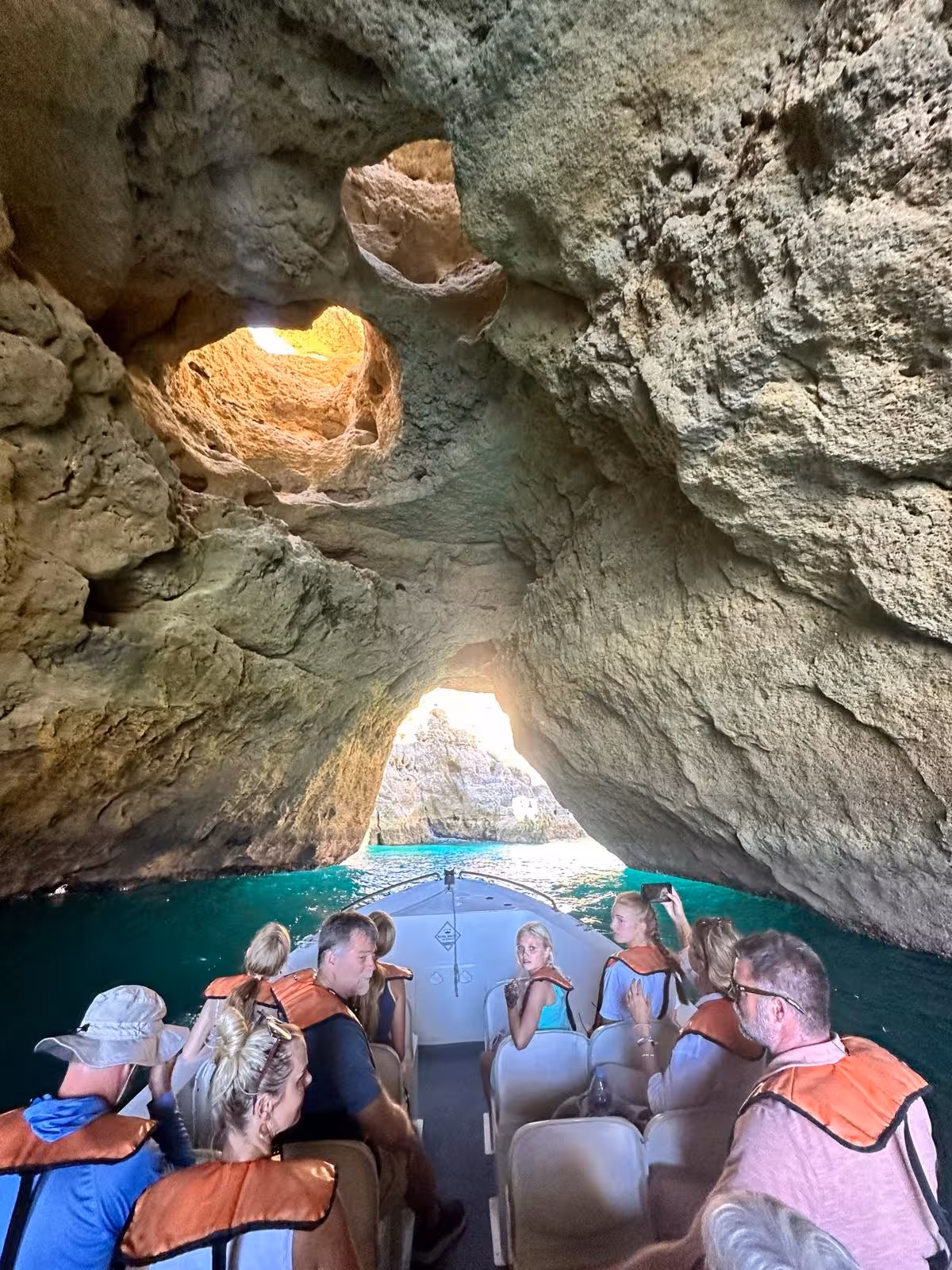 Tourists on a Benagil Caves boat tour glide through a narrow Algarve sea cave tunnel with turquoise water and rugged rock ceiling