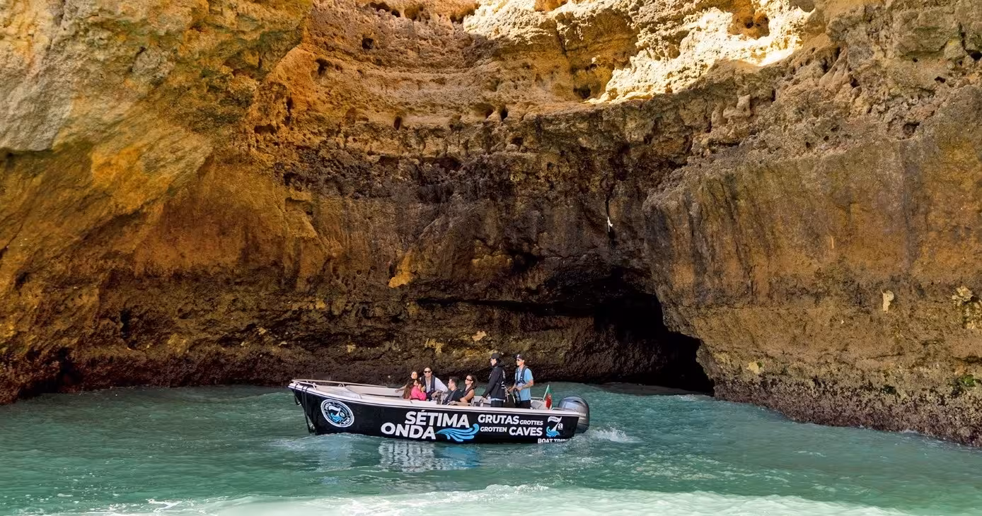 Tourists on a classic Benagil caves boat tour sailing into a dramatic sandstone grotto on Portugal’s Algarve coast