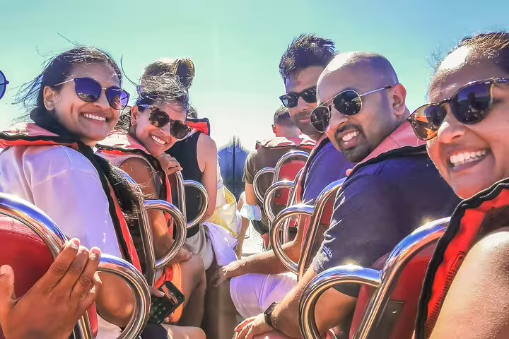 Smiling tourists enjoying a sunny Benagil Caves boat tour during a private Algarve trip from Lisbon, wearing life jackets.