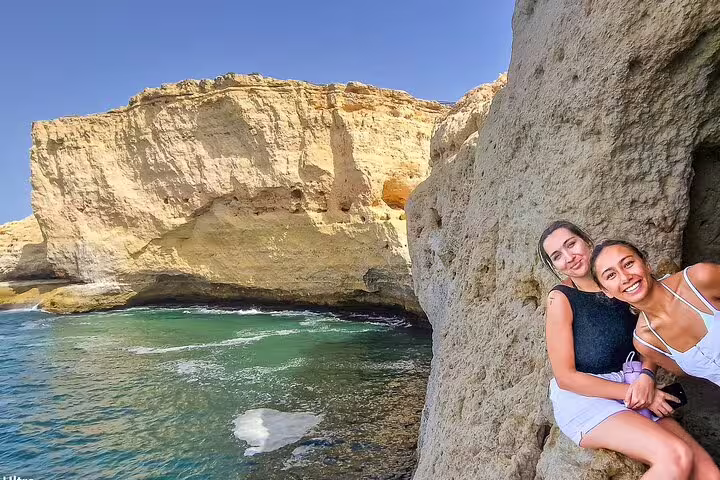 Two smiling tourists enjoy the stunning rock formations and turquoise waters on a boat trip to Benagil caves in Algarve.