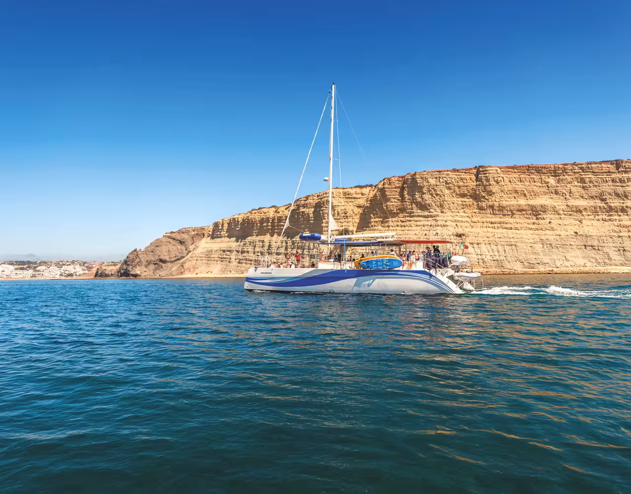 A catamaran sailing past towering golden cliffs on a Portimao Benagil Caves boat tour in the Algarve Portugal