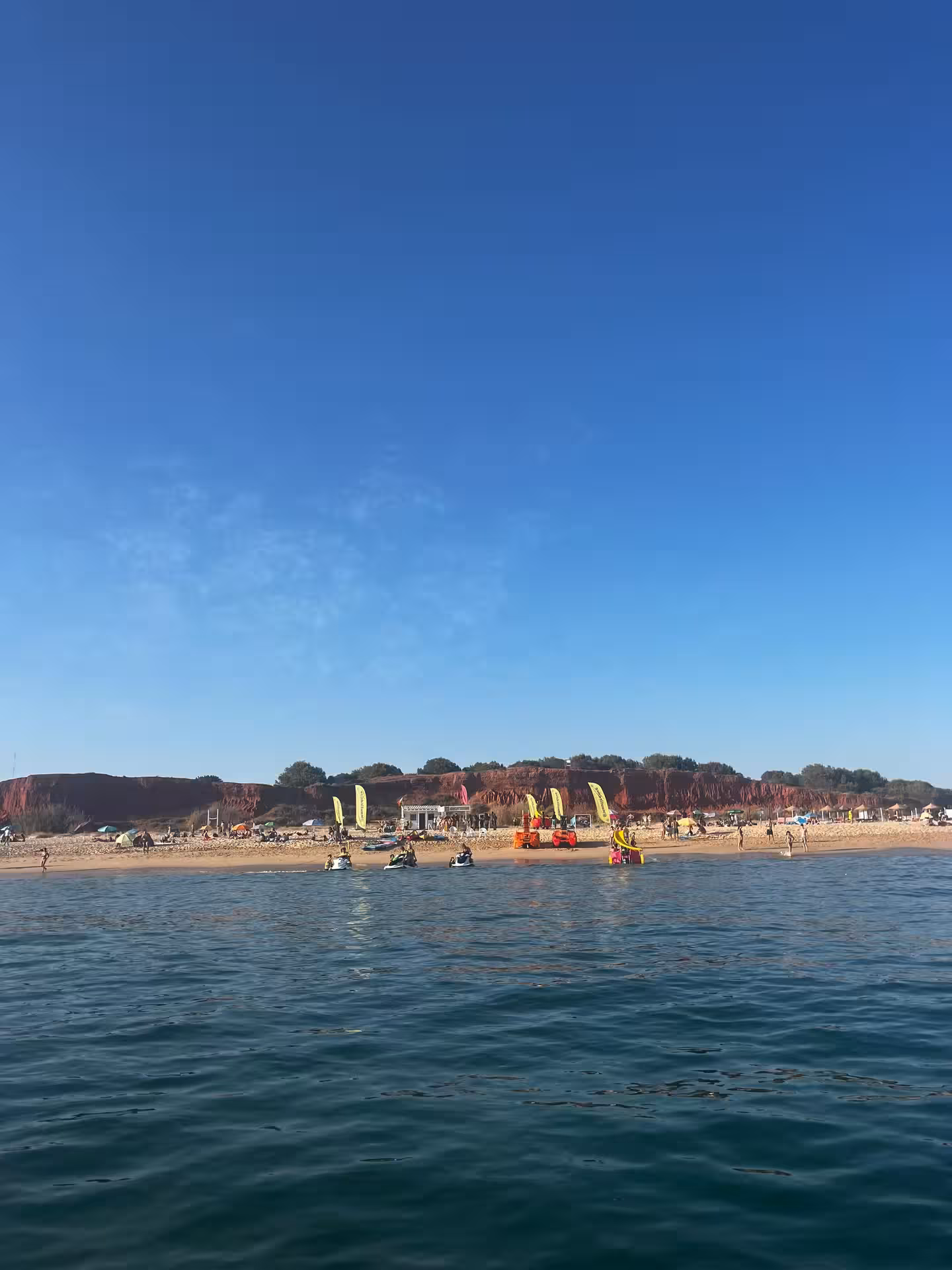 Sunny Algarve beach with tour boats and jet skis ready for Benagil caves and dolphin watching excursion from shore