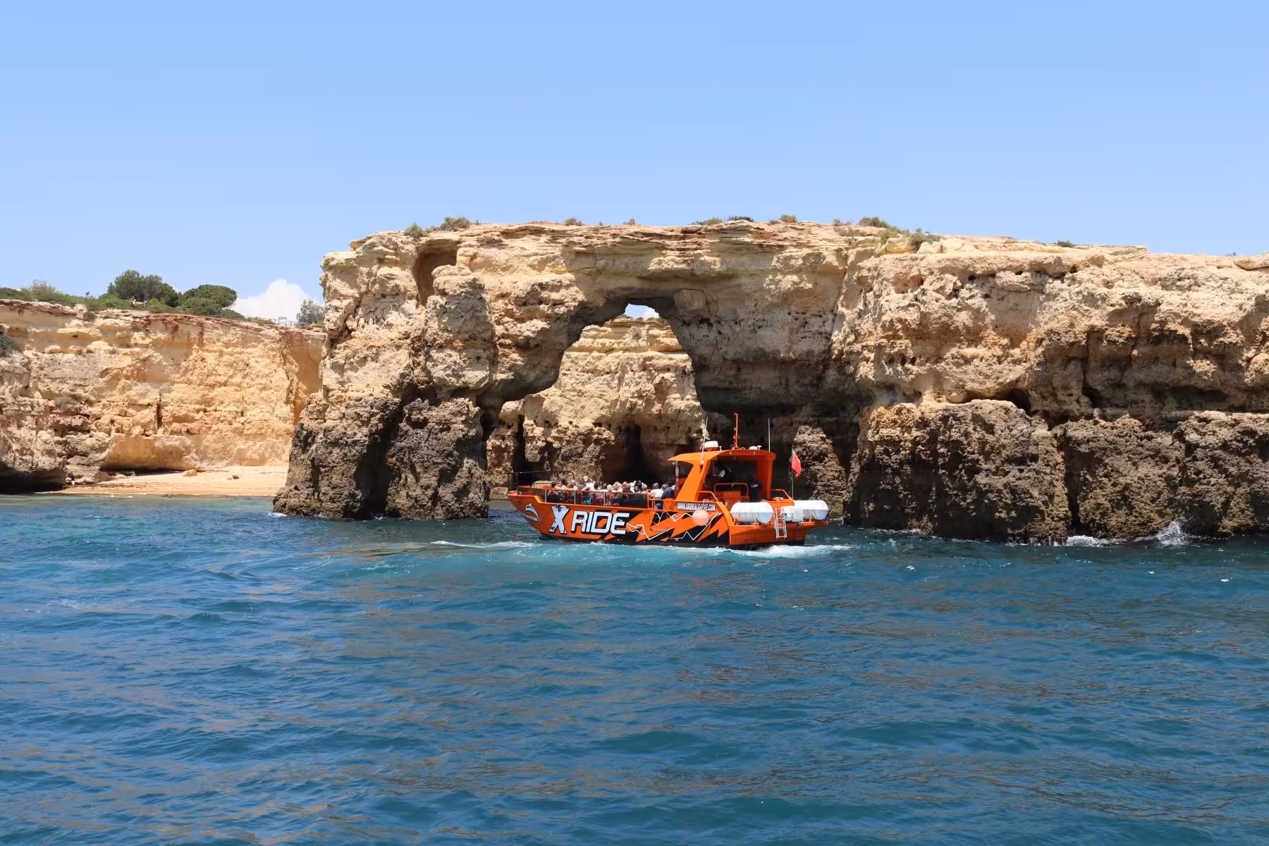 X Ride Benagil caves and dolphins cruise boat passes dramatic Algarve sea arch cliffs on a sunny Portugal coast tour