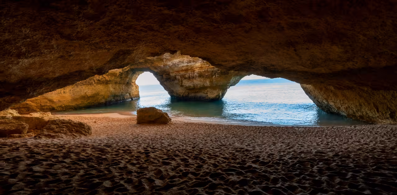 Golden sand beach and calm Atlantic water framed by the natural arches inside Portugal’s famous Benagil sea cave
