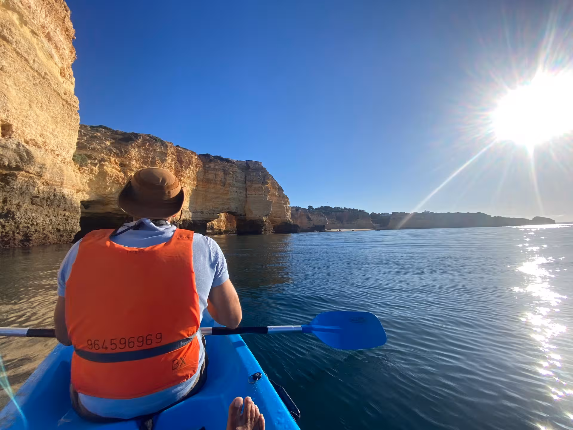 Kayaker in life jacket paddling toward golden Benagil sea caves at sunset on a calm Algarve coast kayak excursion